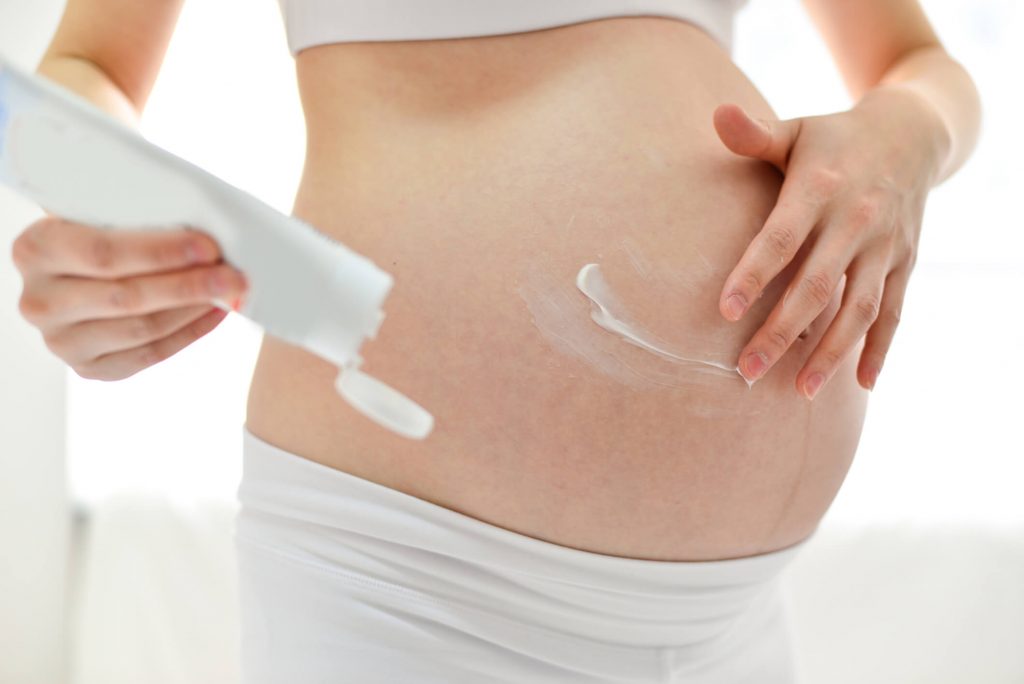 Pregnant woman applying cream toher skin