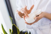 Woman taking some moisturizer from a jar to keep her skin well-hydrated