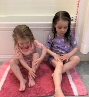 Young sisters lathering moisturizing cream on their legs after bath