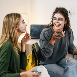 two teenage girls laughing while applying skin care on their face 